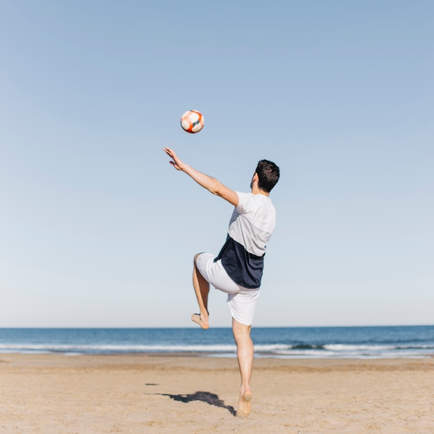 Junger Mann, der Fußball am Strand spielt