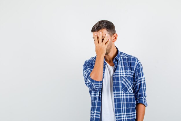 Junger Mann, der Gesicht versteckt Hand im Hemd und Blick verärgert, Vorderansicht.