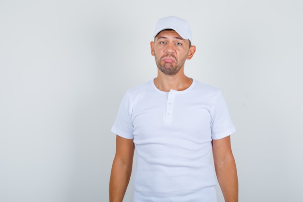 Kostenloses Foto junger mann, der gesichtsausdruck mit lippen in weißem t-shirt, mütze und verwirrtem blick von vorne zeigt.