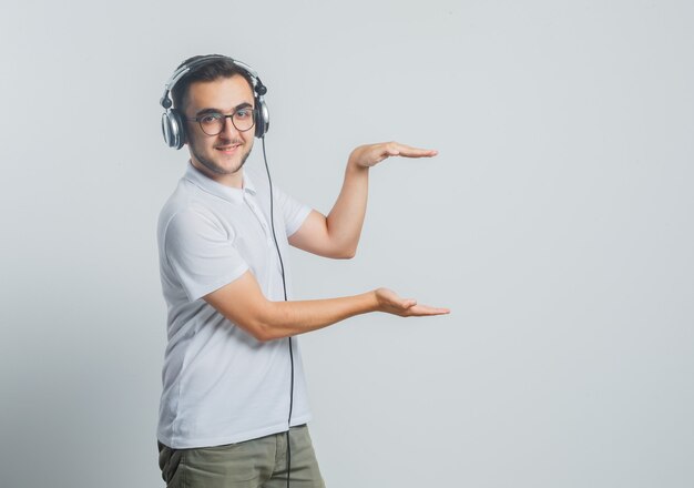 Junger Mann, der Größenzeichen im weißen T-Shirt, in der Hose und im Selbstbewusstsein zeigt