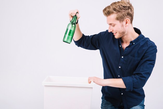 Junger Mann, der grüne Flasche im Mülleimer wirft