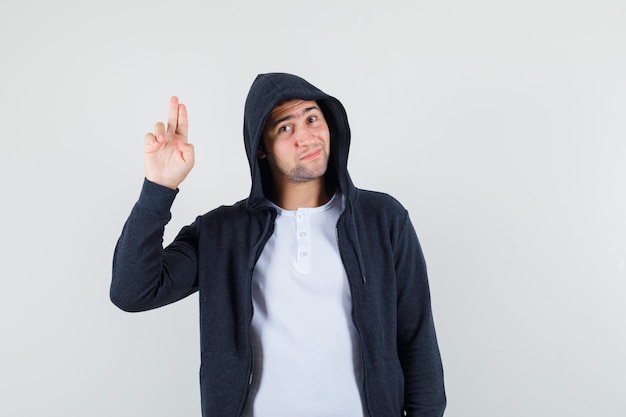 Junger Mann, der Grußgeste in T-Shirt, Jacke zeigt und selbstbewusst aussieht. Vorderansicht.