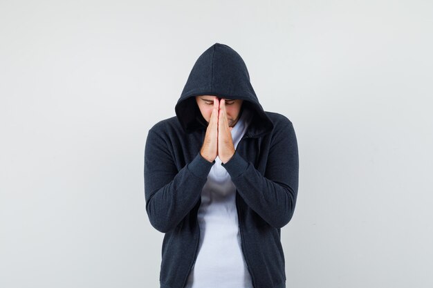 Junger Mann, der Hände in der Gebetsgeste in der Jacke, im T-Shirt hält und hoffnungsvoll aussieht. Vorderansicht.