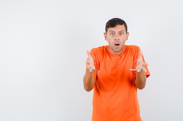 Junger Mann, der Hände in fragender Geste im orangefarbenen T-Shirt erhebt und ratlos aussieht