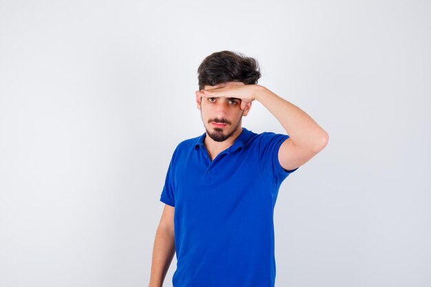 Junger Mann, der Hand auf der Stirn im blauen T-Shirt hält und ernst schaut