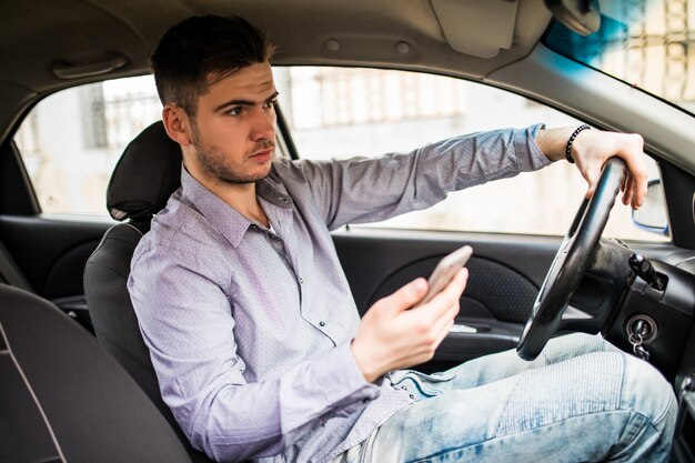 Junger Mann, der Handy beim Autofahren betrachtet.