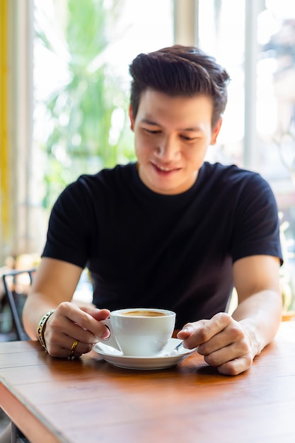 Junger Mann, der heißen Kaffee in der weißen Schale schaut