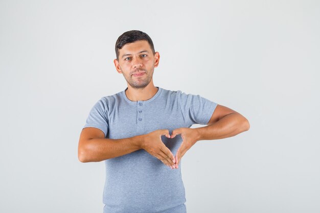 Junger Mann, der Herzgeste mit den Fingern im grauen T-Shirt macht