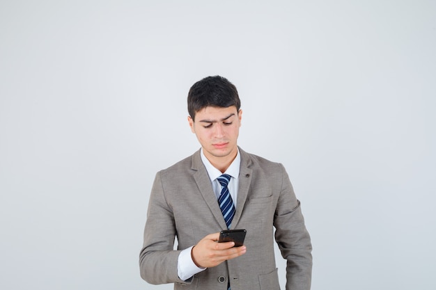 Junger Mann, der im Anzug auf das Telefon schaut