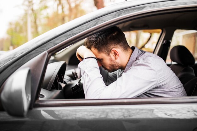 Junger Mann, der im Auto sehr verärgert und gestresst nach schwerem Versagen sitzt und sich im Stau bewegt