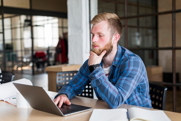 Junger Mann, der im Büro unter Verwendung des Laptops sitzt