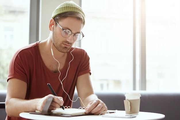 Junger Mann, der im Café sitzt, das Musik hört