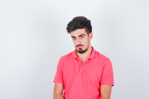 Junger Mann, der im rosa T-Shirt schaut und selbstbewusst aussieht. Vorderansicht.