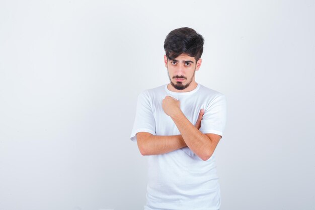 Junger Mann, der im T-Shirt die Faust auf der Brust hält und selbstbewusst aussieht, Vorderansicht.