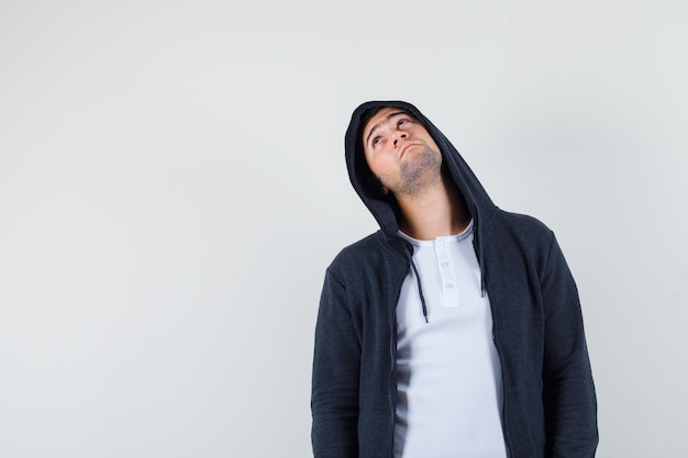 Junger Mann, der im T-Shirt, in der Jacke und in der nachdenklichen Vorderansicht nach oben schaut.