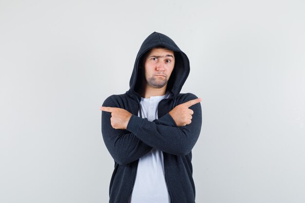 Junger Mann, der im T-Shirt, in der Jacke weg zeigt und unentschlossen schaut, Vorderansicht.