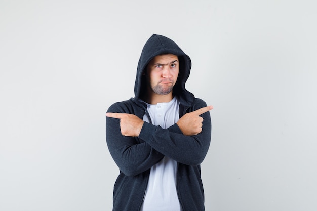 Junger Mann, der im T-Shirt, in der Jacke weg zeigt und zögernd aussieht. Vorderansicht.