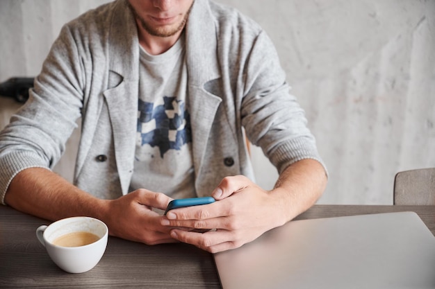 Junger Mann, der im Telefon mit Tasse Kaffee arbeitet