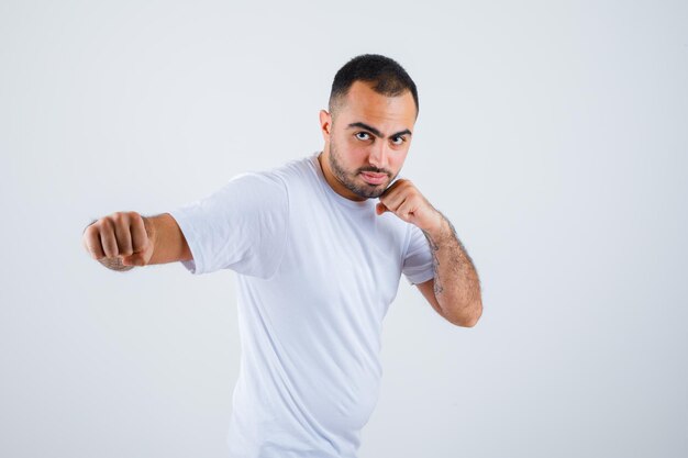 Junger Mann, der in Boxerpose im weißen T-Shirt steht und ernst aussieht