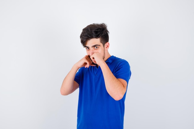 Junger Mann, der in Boxerpose in blauem T-Shirt steht und ernst aussieht