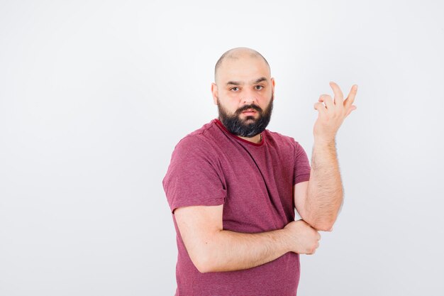 Junger Mann, der in denkender Pose im rosa T-Shirt steht und nachdenklich aussieht. Vorderansicht.