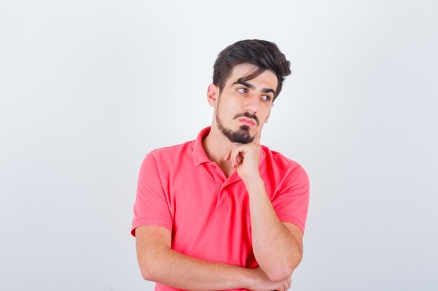 Junger Mann, der in denkender Pose im T-Shirt steht und vernünftig aussieht, Vorderansicht.