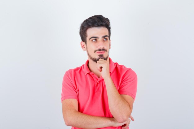 Junger Mann, der in denkender Pose im T-Shirt steht und vernünftig aussieht, Vorderansicht.