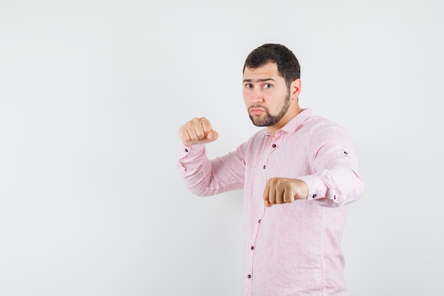 Junger mann, der in der boxerhaltung im rosa hemd steht und stark schaut