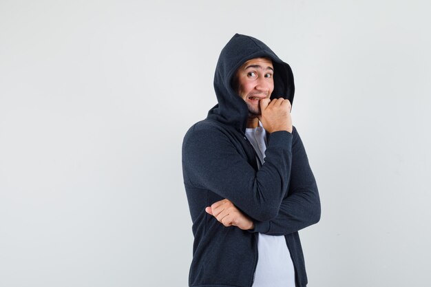 Junger Mann, der in der denkenden Pose im T-Shirt, in der Jacke und in der aufgeregten Vorderansicht steht.