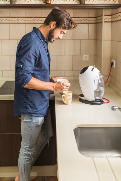 Junger Mann, der in der Küche zubereitet Kaffee steht