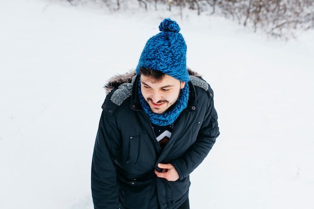 Junger Mann, der in der Winterkleidung auf Schnee steht