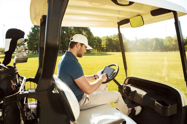 Kostenloses Foto junger mann, der in einem golfwagen mit einer tablette sitzt