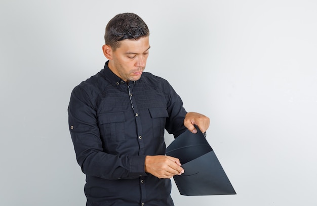 Junger Mann, der in geöffneten Papierumschlag im schwarzen Hemd schaut