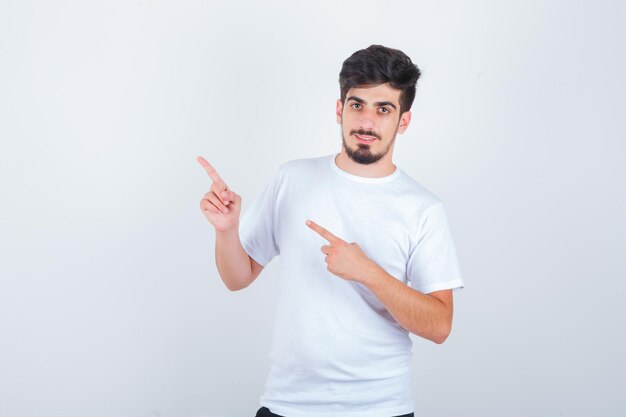 Junger Mann, der in weißem T-Shirt auf die obere linke Ecke zeigt und selbstbewusst aussieht