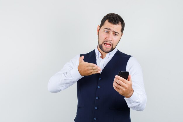 Junger Mann, der jemanden verantwortlich auf Video-Chat im Hemd, Weste hält