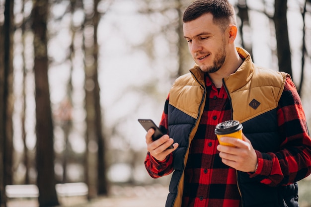 Junger Mann, der Kaffee im Park trinkt und Telefon benutzt