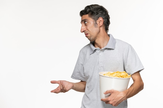 Junger Mann, der Korb der Vorderansicht mit Kartoffelchips hält, spricht mit jemandem auf weißer Oberfläche