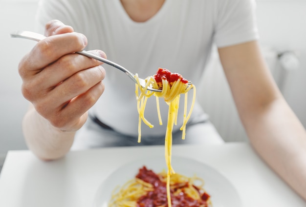 Junger Mann, der leckere Spaghetti mit Tomatensauce isst. Nahansicht.