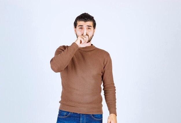Junger Mann, der legere Kleidung trägt und bittet, mit dem Finger auf den Lippen auf weißem Hintergrund ruhig zu sein. Foto in hoher Qualität