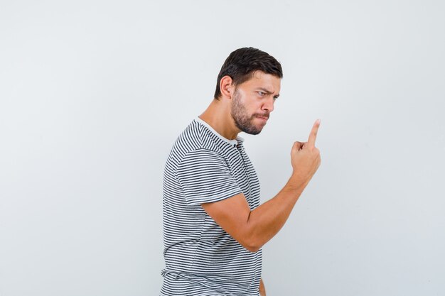 Junger Mann, der mit dem Finger im T-Shirt warnt und wütend aussieht, Vorderansicht.