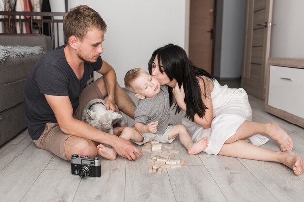 Junger Mann, der mit dem Hund betrachtet ihre Frau küsst seinen Sohn beim Spielen mit Holzklötzen sitzt