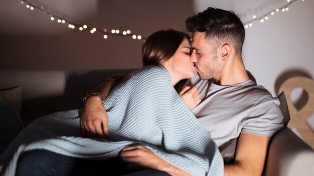 Junger Mann, der mit der Frau liegt auf Sofa küsst