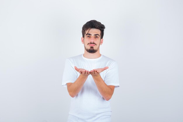 Junger Mann, der mit hohlen Händen im weißen T-Shirt steht und selbstbewusst aussieht