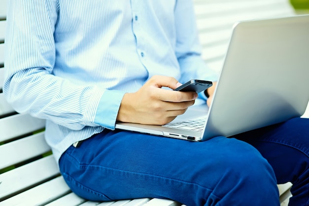 Junger Mann, der mit Laptop, Mannhänden auf Notizbuchcomputer, Geschäftsmann in der Freizeitkleidung in der Straße arbeitet