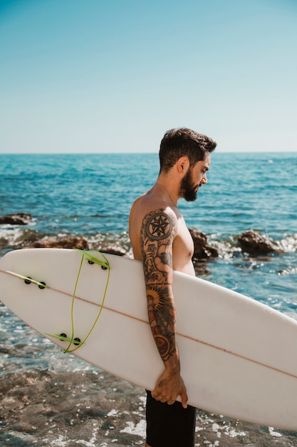 Kostenloses Foto junger mann, der mit surfbrett auf strand steht