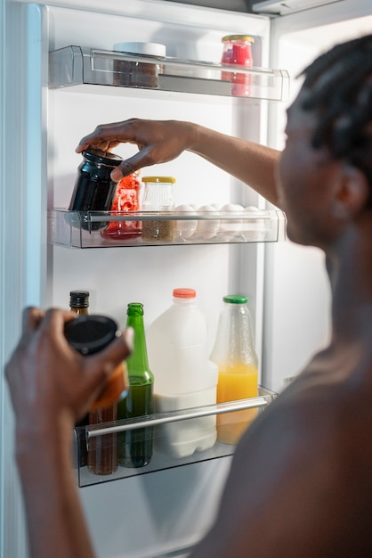 Junger Mann, der mitten in der Nacht zu Hause neben dem Kühlschrank einen Snack isst