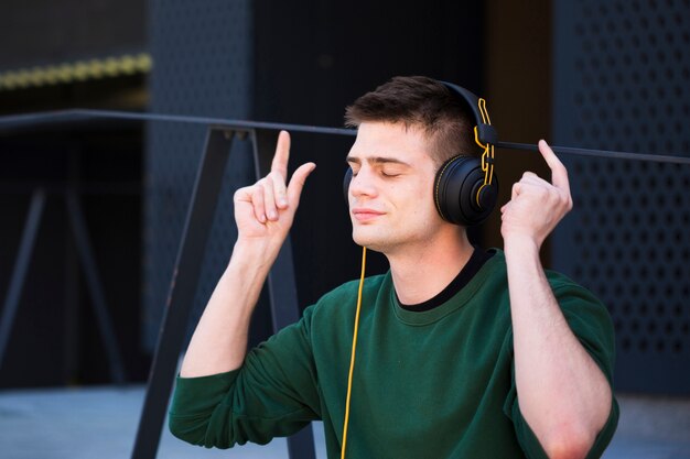 Junger Mann, der Musik in den Kopfhörern mit den angehobenen Händen hört