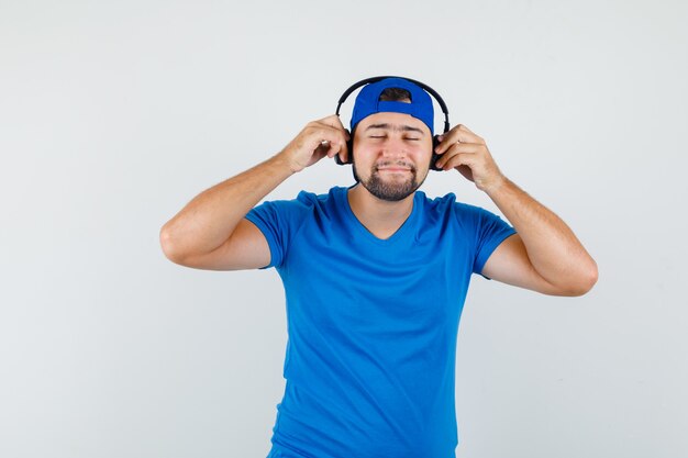 Junger Mann, der Musik mit Kopfhörern im blauen T-Shirt und in der Kappe genießt und entspannt schaut