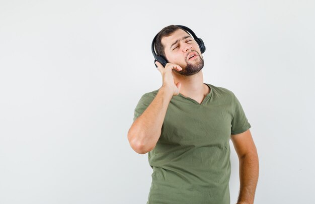 Junger Mann, der Musik mit Kopfhörern im grünen T-Shirt genießt und beschwipst aussieht