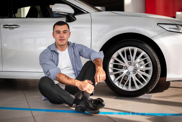 Junger Mann, der nahe bei einem Auto an der Verkaufsstelle sitzt